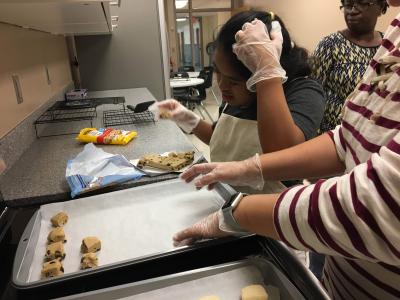 A student and teacher putting raw cookie dough on cookie sheets 